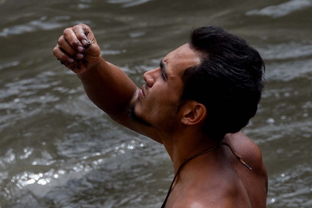 Un hombre mira un objeto que encontró después de recoger el lodo del fondo de un canal de aguas residuales mientras busca metales valiosos en el río Guaire, en Caracas, el 1 de febrero de 2018. Decenas de jóvenes buscan diariamente joyas perdidas en Guaire. Río, donde las alcantarillas de Caracas drenan. Encontrar oro es su ilusión, pero una pieza de alambre de cobre es suficiente para paliar el hambre. / AFP PHOTO / FEDERICO PARRA