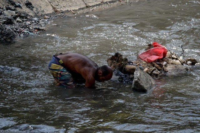 Un hombre saca barro del fondo de un canal de alcantarillado mientras busca metales valiosos en el río Guaire, en Caracas, el 1 de febrero de 2018. Decenas de jóvenes buscan diariamente joyas perdidas en el río Guaire, donde drenan las alcantarillas de Caracas. . Encontrar oro es su ilusión, pero una pieza de alambre de cobre es suficiente para paliar el hambre. / AFP PHOTO / FEDERICO PARRA