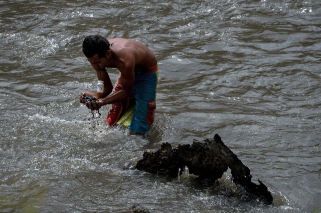 Un hombre saca barro del fondo de un canal de alcantarillado mientras busca metales valiosos en el río Guaire, en Caracas, el 1 de febrero de 2018. Decenas de jóvenes buscan diariamente joyas perdidas en el río Guaire, donde drenan las alcantarillas de Caracas. . Encontrar oro es su ilusión, pero una pieza de alambre de cobre es suficiente para paliar el hambre. / AFP PHOTO / FEDERICO PARRA