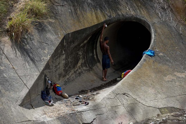 Un hombre fuma un cigarrillo mientras toma un descanso después de buscar metales valiosos en un canal de alcantarillado en el río Guaire, en Caracas, el 1 de febrero de 2018. Decenas de jóvenes buscan diariamente joyas perdidas en el río Guaire, donde drena el alcantarillado de Caracas. Encontrar oro es su ilusión, pero una pieza de alambre de cobre es suficiente para paliar el hambre. / AFP PHOTO / FEDERICO PARRA