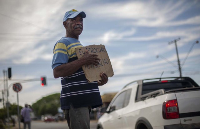 Venezuelan wall painter Jose Ojeda, 52, walks in a traffic light asking for a job with a cardboard sign reading "I look for a job" in the city of Boa Vista, Roraima, Brazil, on February 26, 2018. When the Venezuelan migratory flow exploded in 2017 the city of Boa Vista, the capital of the state of Roraima, 200 kilometers from the Venezuelan border, began to set up shelters as people started to settle in squares, parks and corners of this city of 330,000 inhabitants of which 10 percent is now Venezuelan. / AFP PHOTO / MAURO PIMENTEL