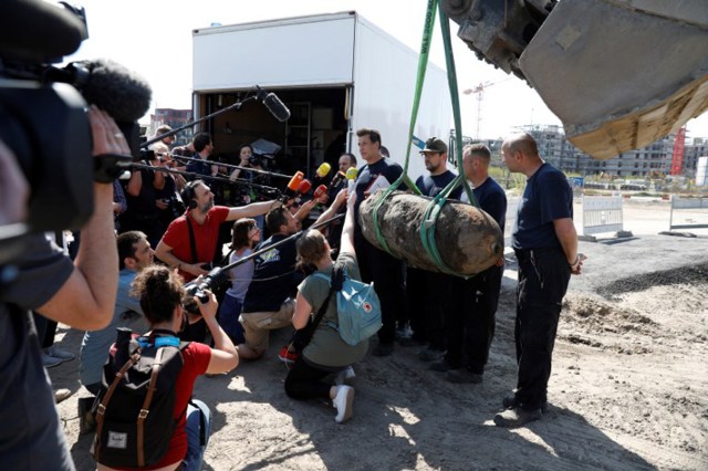 Un miembro de la policía alemana responde las preguntas de los periodistas al lado de una bomba lanzada durante la Segunda Guerra Mundial, ya que se levanta con una excavadora durante la operación de eliminación el 20 de abril de 2018 en Berlín. Miles de personas alrededor de la estación central de trenes de Berlín fueron evacuados mientras los expertos en desactivación de explosivos desactivaron un explosivo sin explotar de la Segunda Guerra Mundial desenterrado en una obra en el distrito Mitte de Berlín. / AFP PHOTO / Odd ANDERSEN