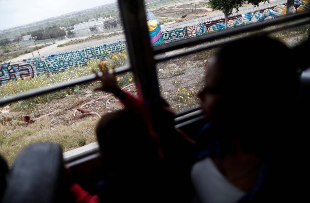 Members of a caravan of migrants from Central America ride on a bus past the border fence between Mexico and the U.S., to gather in a park prior to preparations for an asylum request in the U.S., in Tijuana, Mexico April 29, 2018. REUTERS/Edgard Garrido