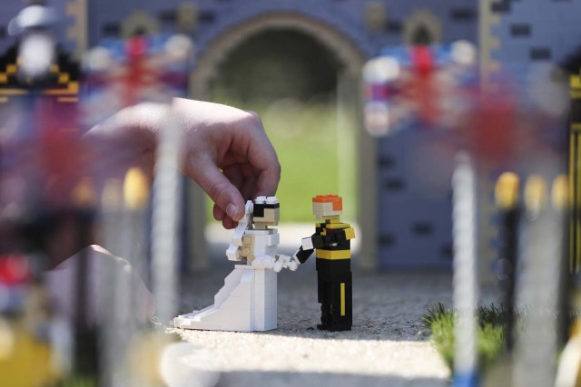 Legoland employee, Lucy, poses putting a Lego model of US actress Meghan Markle (L) in place next to her husband-to-be Britain's Prince Harry (R) outside a Lego-brick model of Windsor Castle at Legoland in Windsor on May 8, 2018 during a photo call for its attraction celebrating the upcoming royal wedding. Prince Harry and US actress Meghan Markle will marry on May 19 at St. George's Chapel at Windsor Castle. / AFP PHOTO / Daniel LEAL-OLIVAS