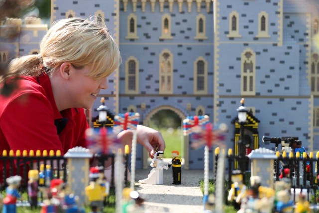 Legoland employee, Lucy, poses putting a Lego model of US actress Meghan Markle (L) in place next to her husband-to-be Britain's Prince Harry (R) outside a Lego-brick model of Windsor Castle at Legoland in Windsor on May 8, 2018 during a photo call for its attraction celebrating the upcoming royal wedding. Prince Harry and US actress Meghan Markle will marry on May 19 at St. George's Chapel at Windsor Castle. / AFP PHOTO / Daniel LEAL-OLIVAS