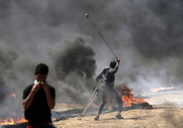 Un palestino usa un tirachinas durante los enfrentamientos con las fuerzas israelíes cerca de la frontera entre Gaza e Israel al este de la ciudad de Gaza el 14 de mayo de 2018, mientras los palestinos protestan por la inauguración de la embajada de Estados Unidos tras su controvertido traslado a Jerusalén. Docenas de palestinos fueron asesinados por disparos israelíes el 14 de mayo cuando decenas de miles protestaron y estallaron enfrentamientos a lo largo de la frontera de Gaza contra la transferencia de su embajada a Jerusalén, luego de meses de protestas globales, ira palestina y elogios exuberantes de los israelíes por el presidente Donald Trump decisión dejando de lado décadas de precedentes. / AFP PHOTO / MAHMUD HAMS