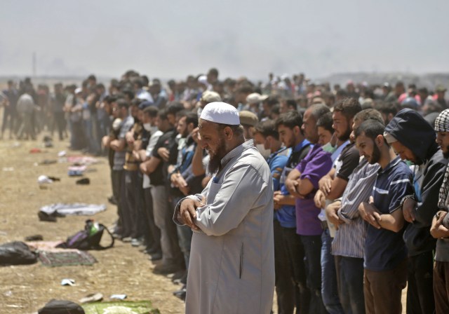 Los palestinos rezan durante los enfrentamientos con las fuerzas israelíes cerca de la frontera entre la franja de Gaza e Israel al este de la ciudad de Gaza el 14 de mayo de 2018, durante una manifestación el día de la mudanza de la embajada de EE. UU. A Jerusalén. Docenas de palestinos fueron asesinados por disparos israelíes el 14 de mayo cuando decenas de miles protestaron y estallaron enfrentamientos a lo largo de la frontera de Gaza contra la transferencia de su embajada a Jerusalén, luego de meses de protestas globales, ira palestina y elogios exuberantes de los israelíes por el presidente Donald Trump decisión dejando de lado décadas de precedentes. / AFP PHOTO / MAHMUD HAMS