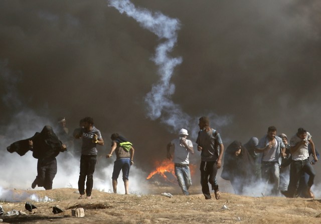 Los palestinos chocan con las fuerzas israelíes cerca de la frontera entre la franja de Gaza e Israel al este de la ciudad de Gaza el 14 de mayo de 2018, mientras los palestinos protestan por la inauguración de la embajada de Estados Unidos tras su controvertido traslado a Jerusalén. Docenas de palestinos fueron asesinados por disparos israelíes el 14 de mayo cuando decenas de miles protestaron y estallaron enfrentamientos a lo largo de la frontera de Gaza contra la transferencia de su embajada a Jerusalén, luego de meses de protestas globales, ira palestina y elogios exuberantes de los israelíes por el presidente Donald Trump decisión dejando de lado décadas de precedentes. / AFP PHOTO / Thomas COEX